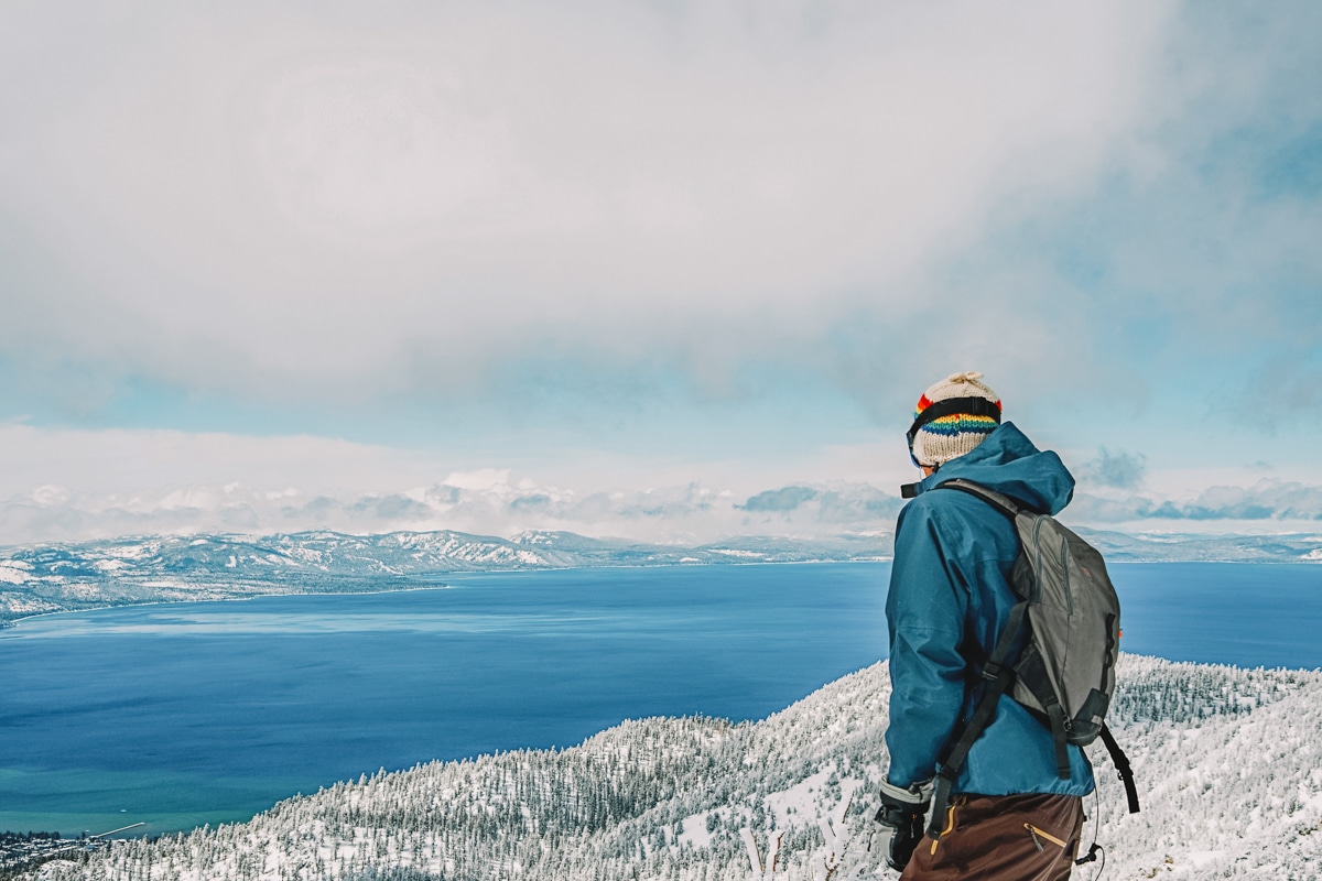 Man in winter gear looking out over a snowy Lake Tahoe.