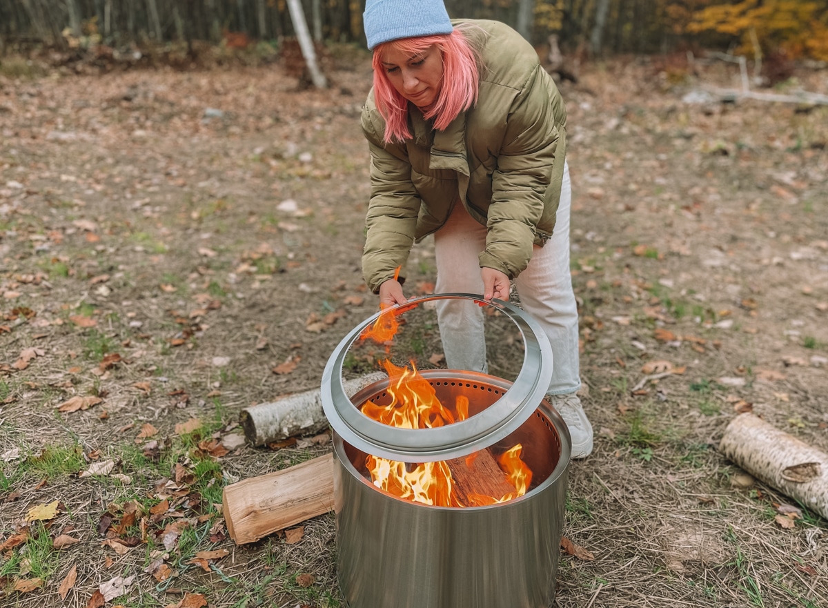 Woman with pink hair placing the fire ring on top of a newly-lit bonfire in a Solo Stove