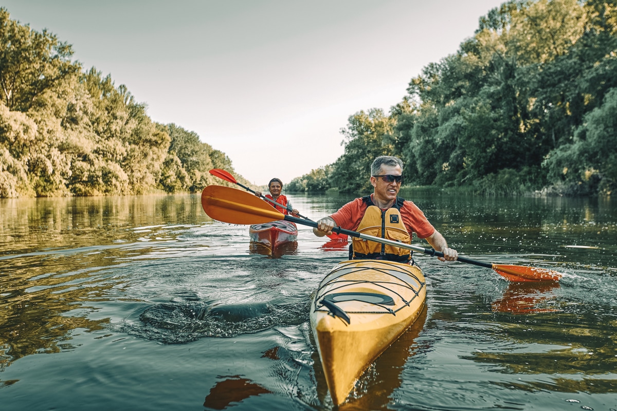 Picture of a man kayaking on a river, best kayak accessories featured image.