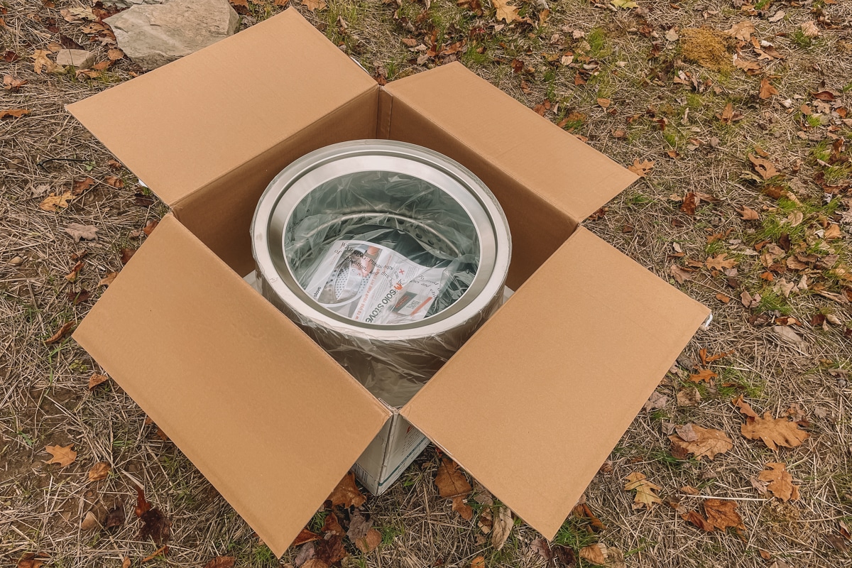 An open Solo Stove box with a brand new Solo Stove inside, sitting on the ground outdoors.