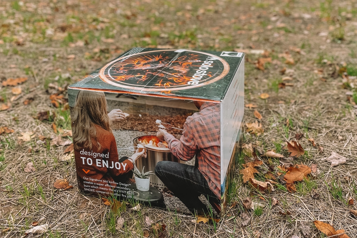 An unopened Solo Stove box sitting on the ground outdoors with fall leaves strewn around.