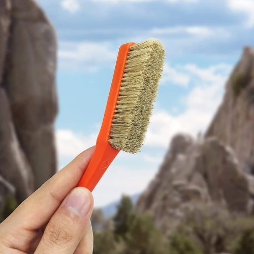TWO STONES Climbing & Bouldering Brush Gift product photo, showing a hand holding up a small orange brush with mountains in the background.