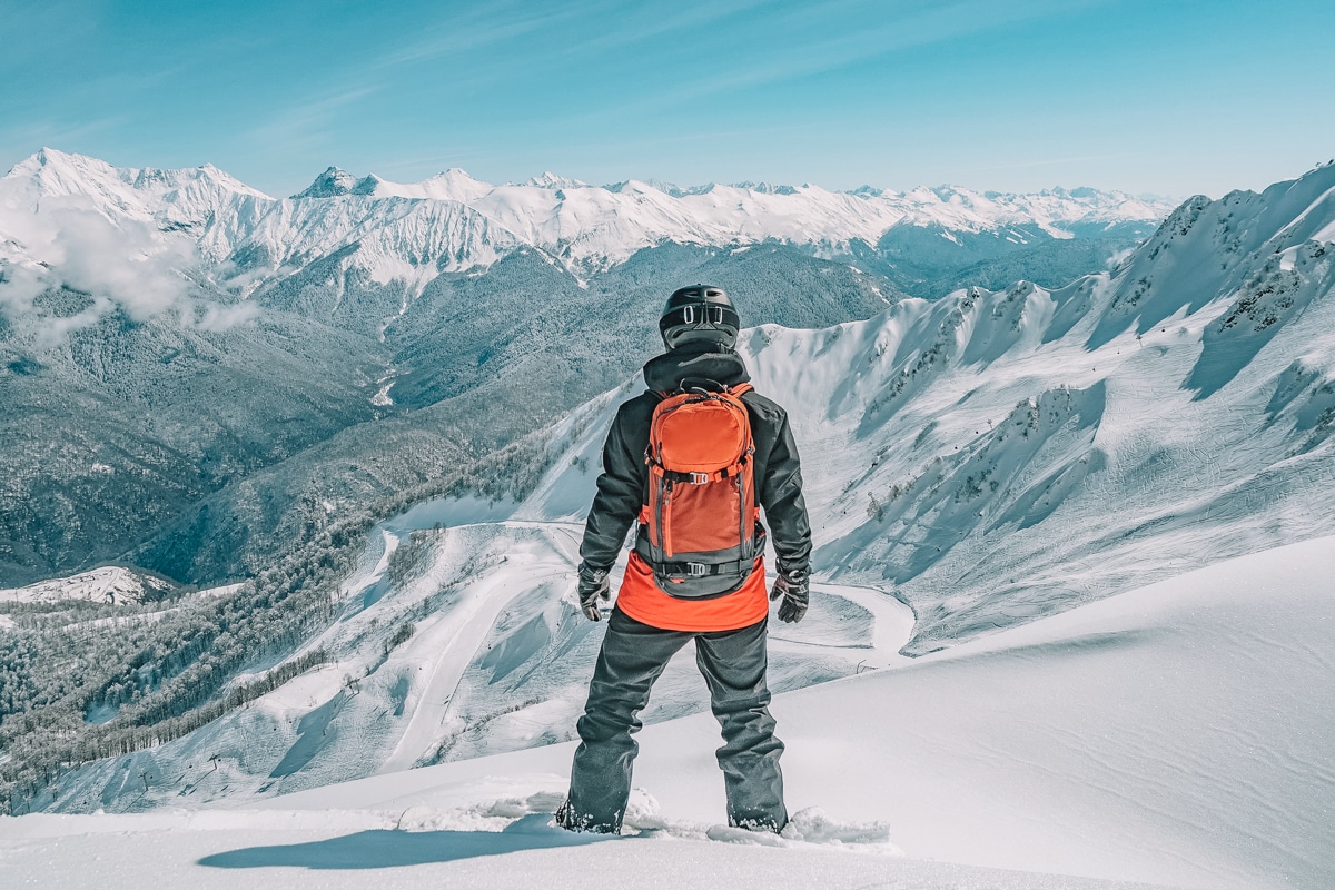 Picture of a snowboarder looking at a beautiful view of the mountains he's about to go down in a ski resort.