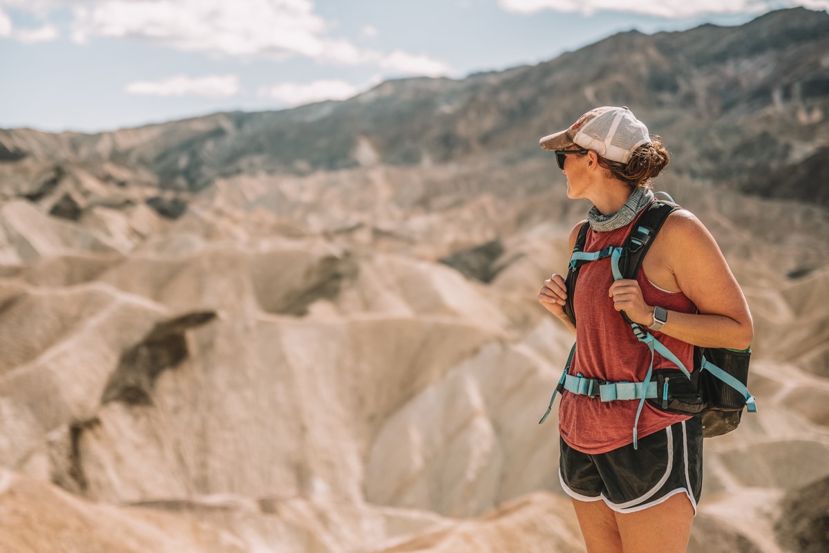 Woman with backpack and red tank top looking out at Death Valley Hills during a winter hike.