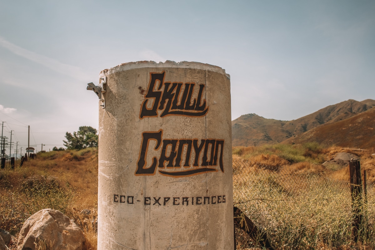 A sign for Skull Canyon Ziplines with a dry grassy landscape in the background.