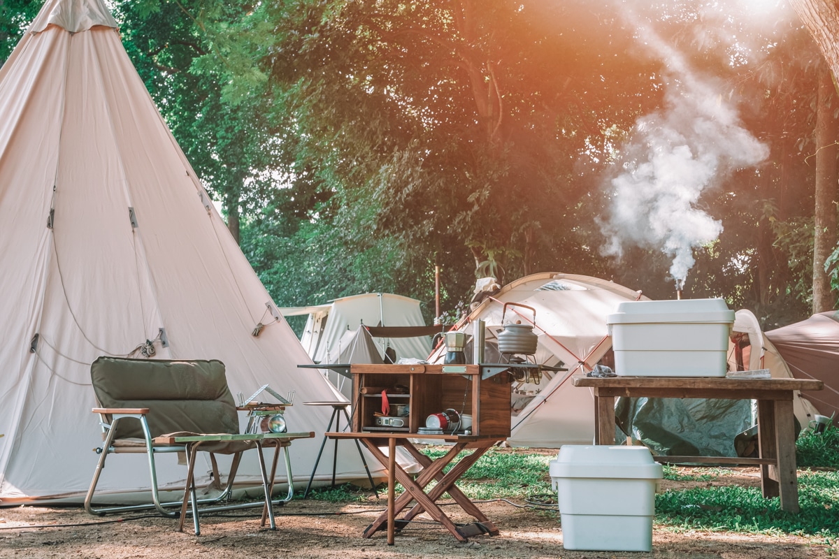 A luxury campsite with a canvas teepee and a folding camping kitchen table, with smoke rising in the background.