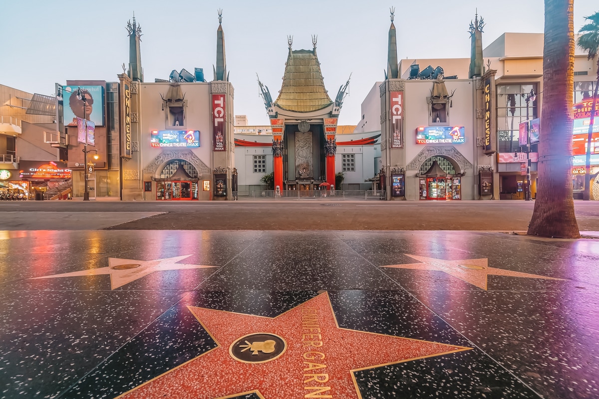 A view of the TCL Chinese Theater surrounded by glowing lights with some Hollywood stars in the foreground. 