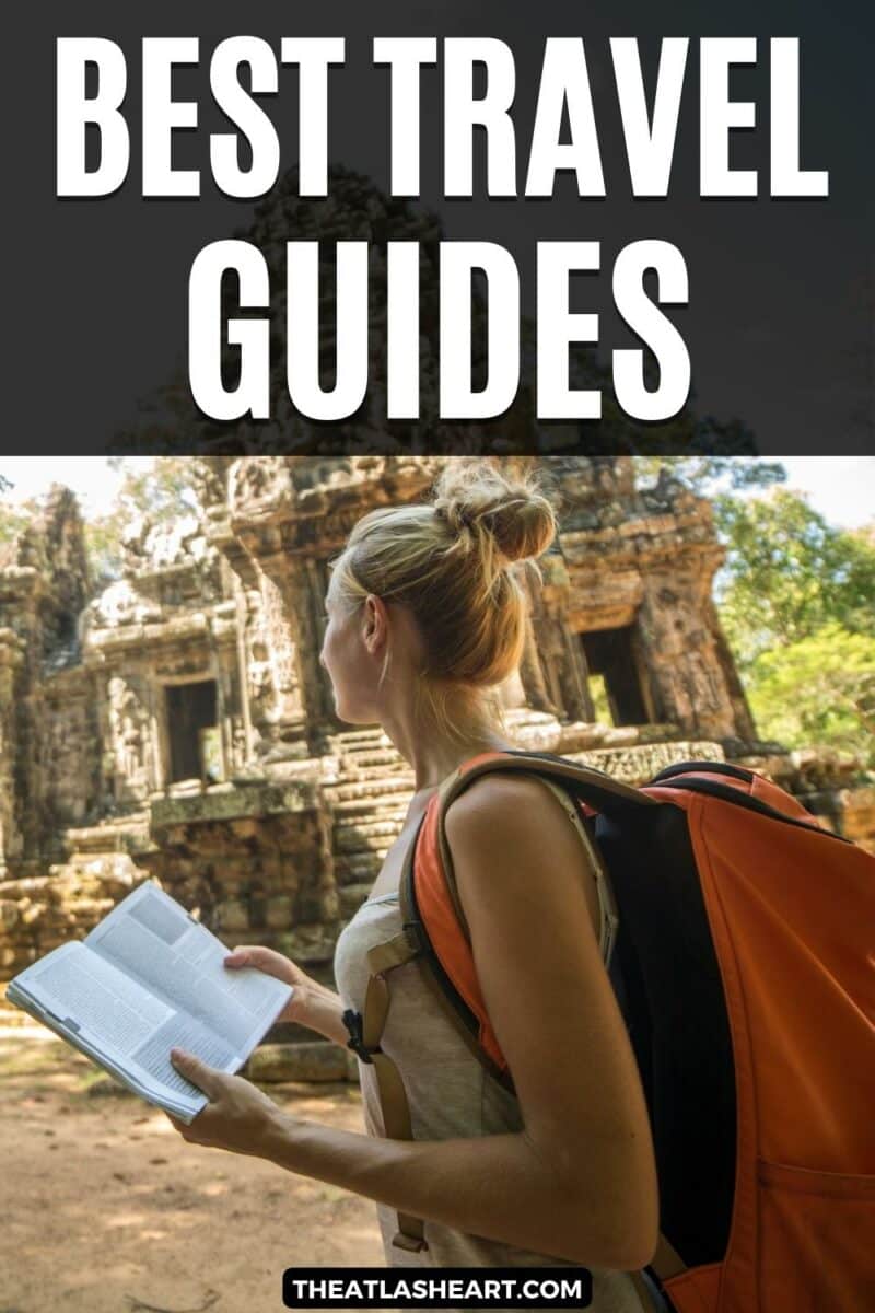 A blonde woman wearing an orange backpack holds an open book while looking at the ruins of a tropical temple, with the text overlay, "Best Travel Guides."