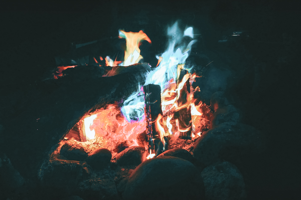 A close-up of a campfire with multi-colored flames burning at night.